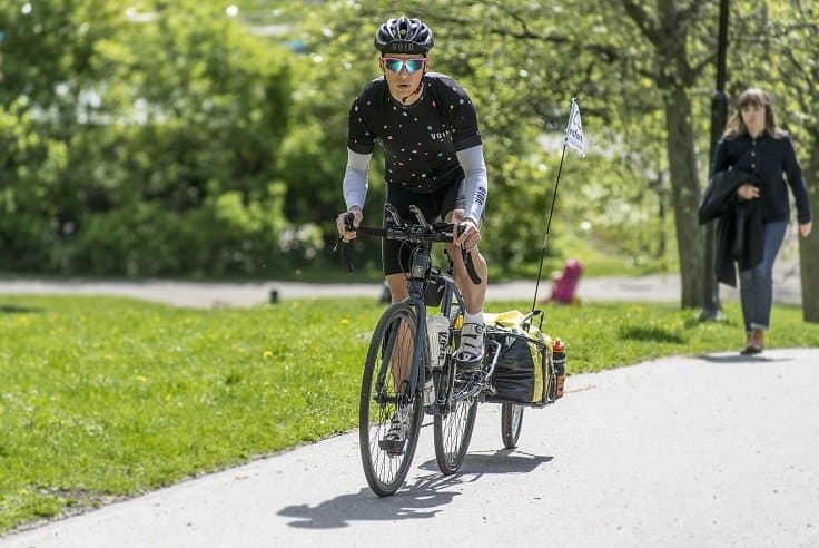 Toni Trajcevski cyklar genom en park i solen.