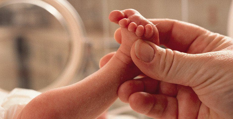 Närbild på en hand som håller i en liten bebisfot.