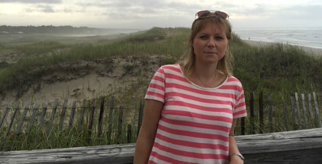 Porträtt av Camilla Lööv med strand och vatten i bakgrunden.