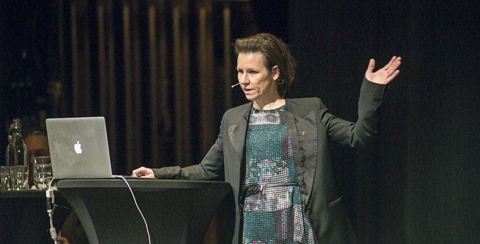 Marie Carlén talar i en mikrofon och pekar med handen.