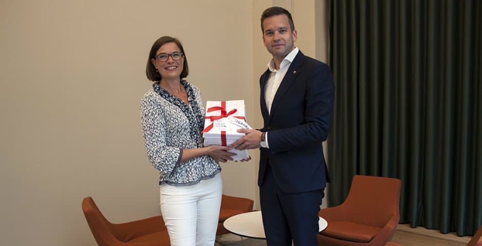 Anna Hemlin och Gabriel Wikström står med en hög av papper som är inslagna med ett rött band.