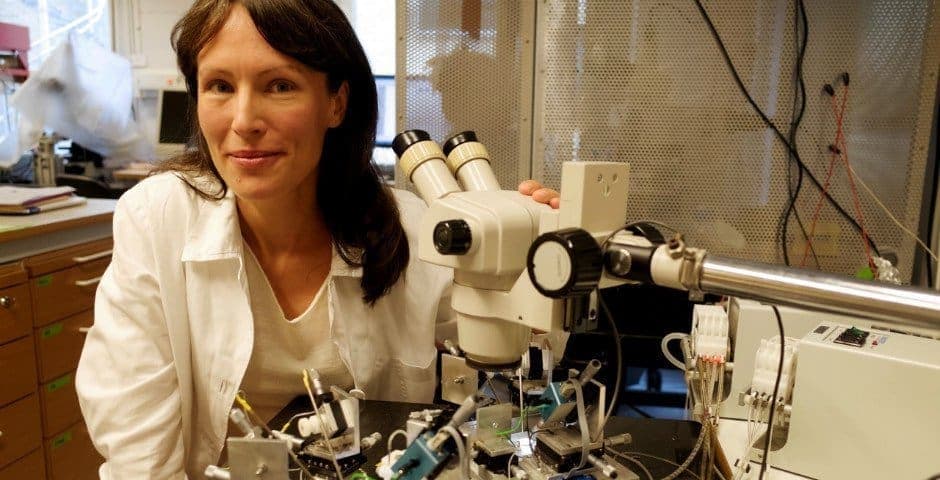 Porträtt av Louise Adermark som sitter vid ett mikroskop.