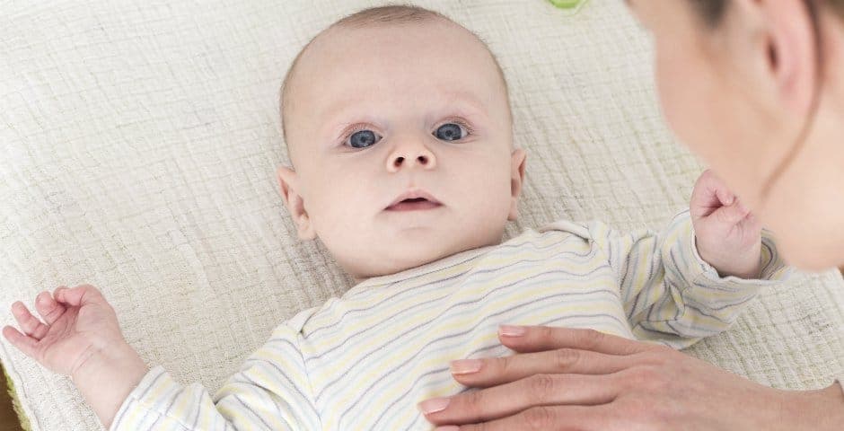 Bebis tittar upp mot kameran och en person som håller sin hand över bebisens mage.