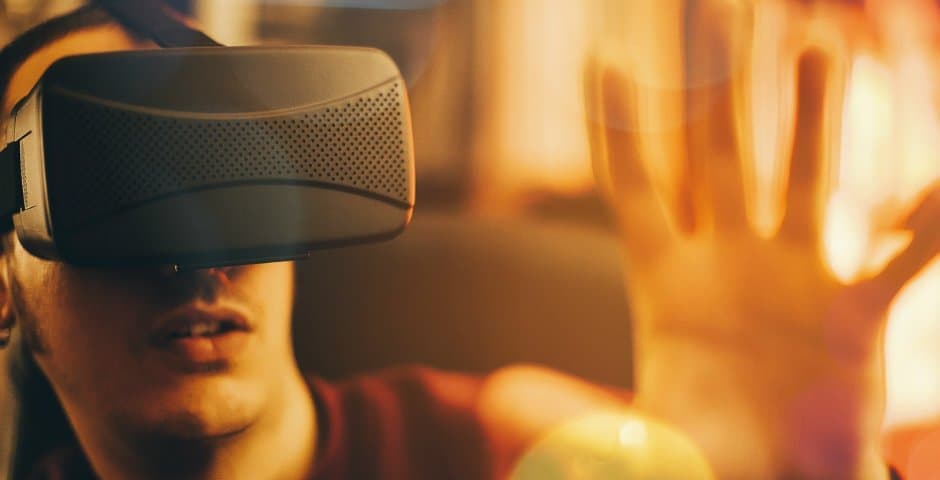 En kille sitter med VR-glasögon med sin hand upplyft.