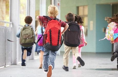 Skolbarn springer med sina skolväskor på ryggen.