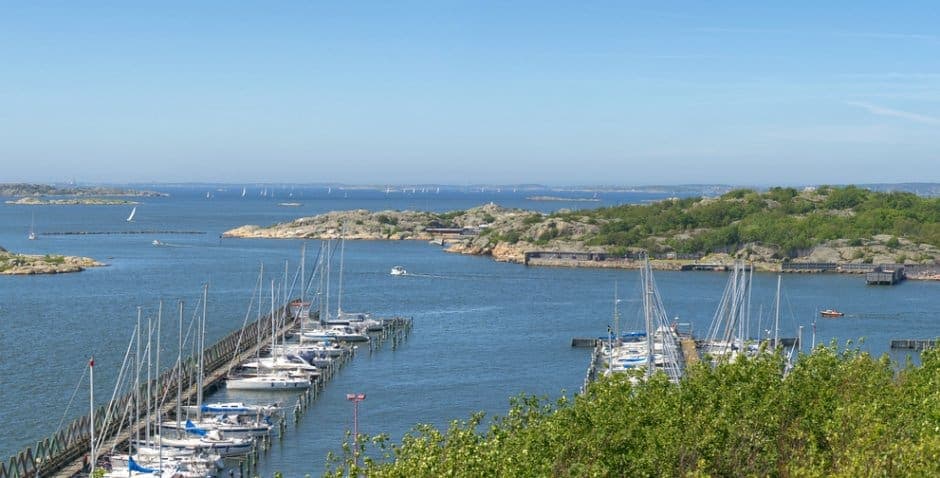 En hamn med flera segelbåtar som ligger i vattnet, samt flera båtar som är ute och seglar.