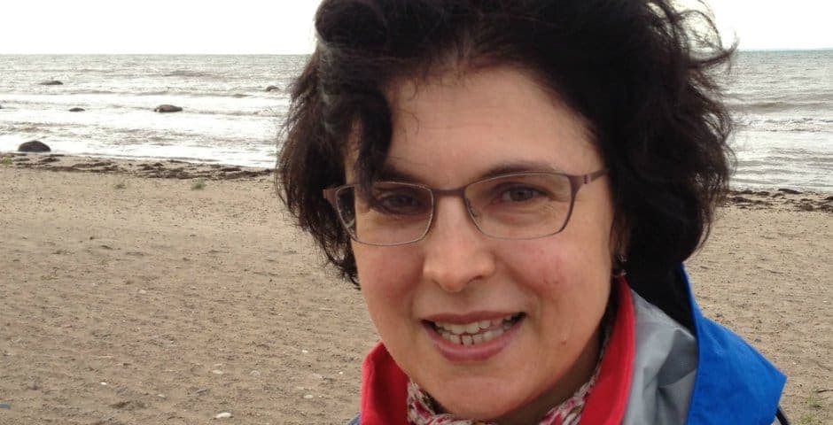 Porträtt av Angela Cenci-Nilsson som står på en strand vid vattnet.