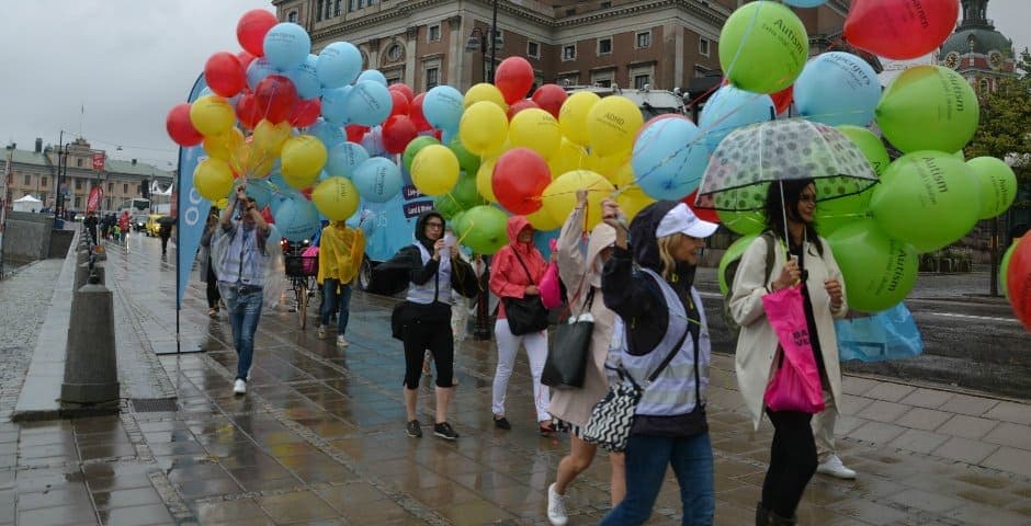 Flera personer går med stora färgglada ballonger som det står olika diagnoser på under Anna Hemlin och Lena Dahlenborg står utomhus med färglada ballonger under Hjärnfondens manifestation.