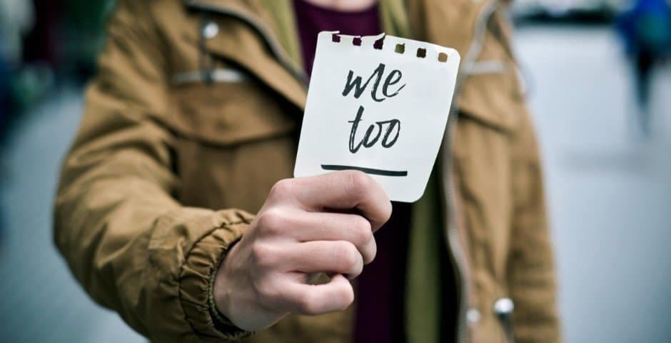 En person som håller upp en lapp med texten "Me too."