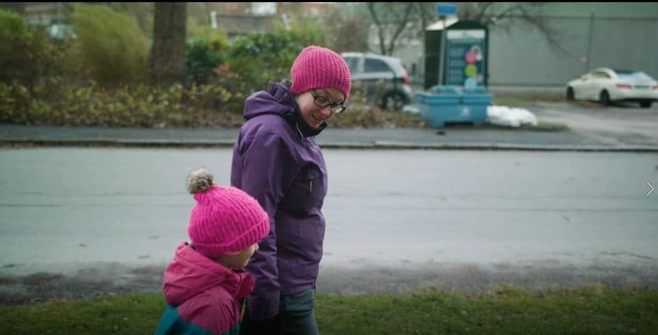 En mamma går med sin dotter hand i hand längs en bilväg.