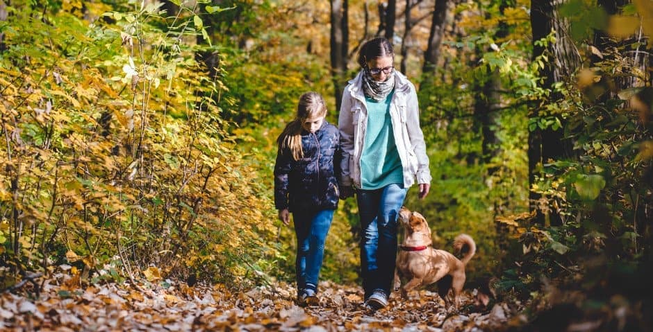 En mamma och en dotter går med en hund ute i skogen.
