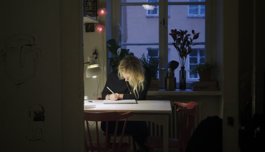 Edith tecknar på ett papper vid ett bord.