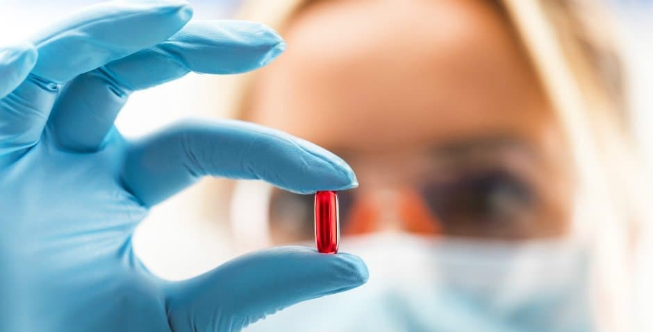 Vårdpersonal håller i ett rött piller.