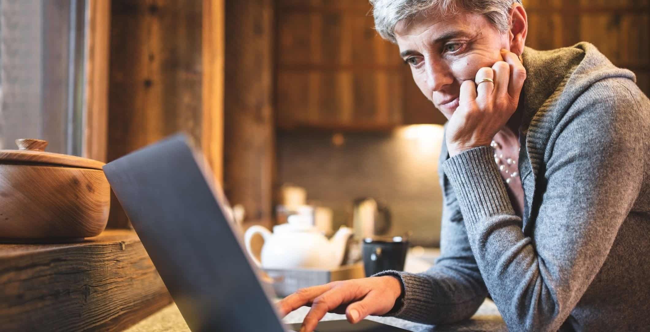 Kvinna sitter i köket med en dator.