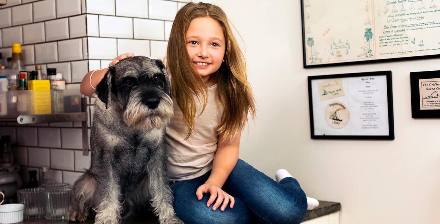 Liten flicka sitter med en hund på en köksbänk.