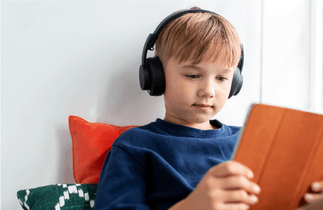 Pojke sitter med en Ipad och hörlurar.