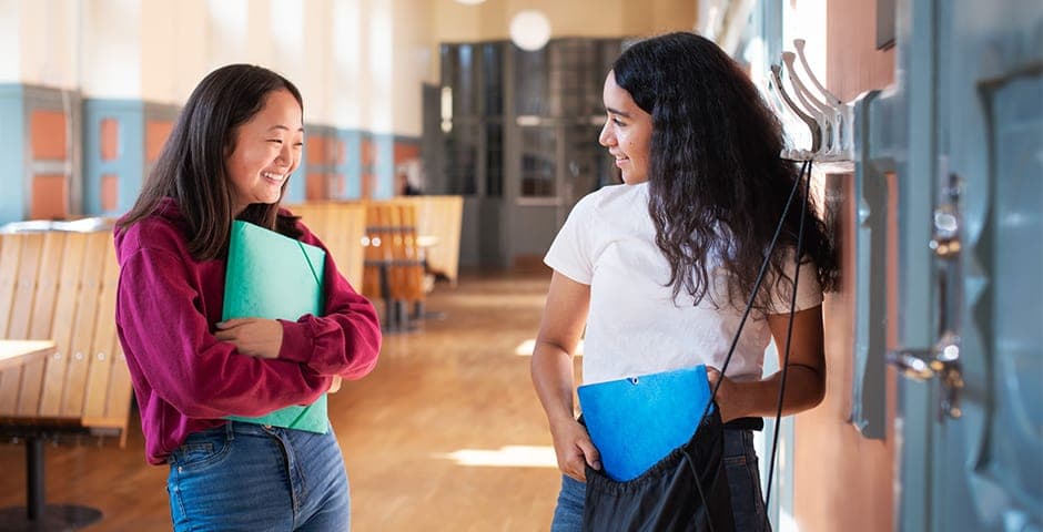 Två tonårstjejer pratar i en skolkorridor.