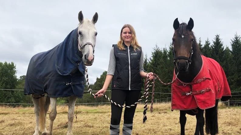 Therese står mellan två hästar i en hage.