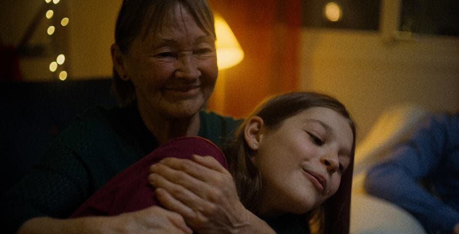 Farmor kramar om sitt barnbarn och sitter i skenet av en lampa.