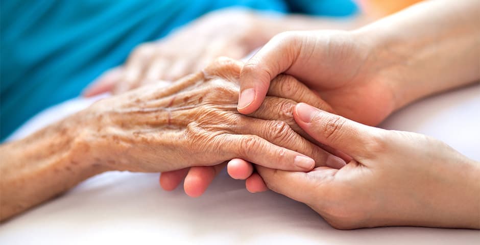 Närbild på ett par händer som håller i en äldre persons hand.