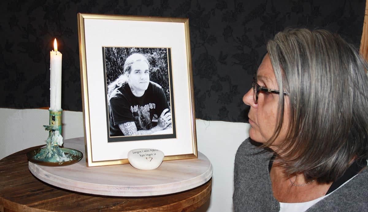 Helen Utbys sitter bredvid ett porträtt av sonen Anders. Bredvid porträttet står ett tänt ljus.