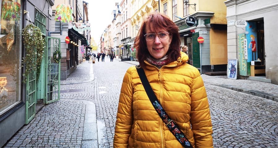 Annsophie i gul jacka ler mot kameran. Hon står i gatumiljö.