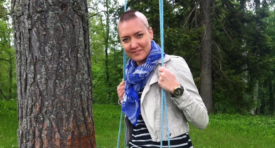 Emma med snaggat hår sitter på en gunga utomhus i en grönskande miljö.
