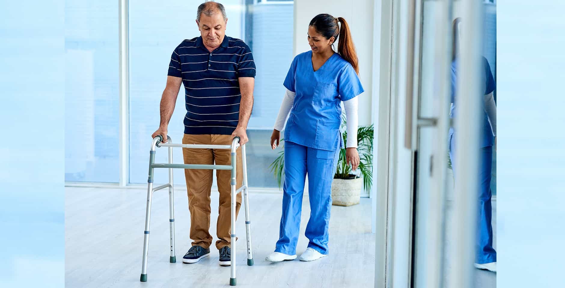 Sjuksköterska hjälper man att gå med hjälp av ett gåstativ.