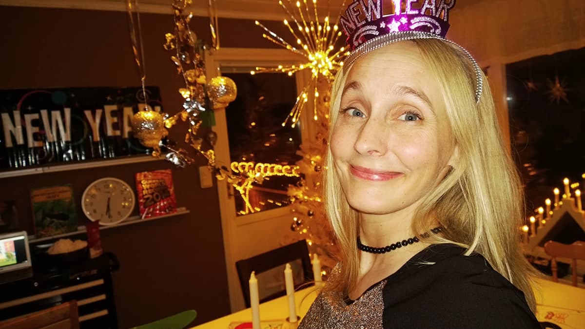 Emelie Vestman ler mot kameran med en nyårshatt i ett rum med nyårsdekoration.