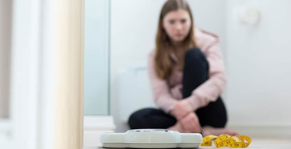 Tonårsflicka sitter på golvet tittar på en våg och ett måttband.