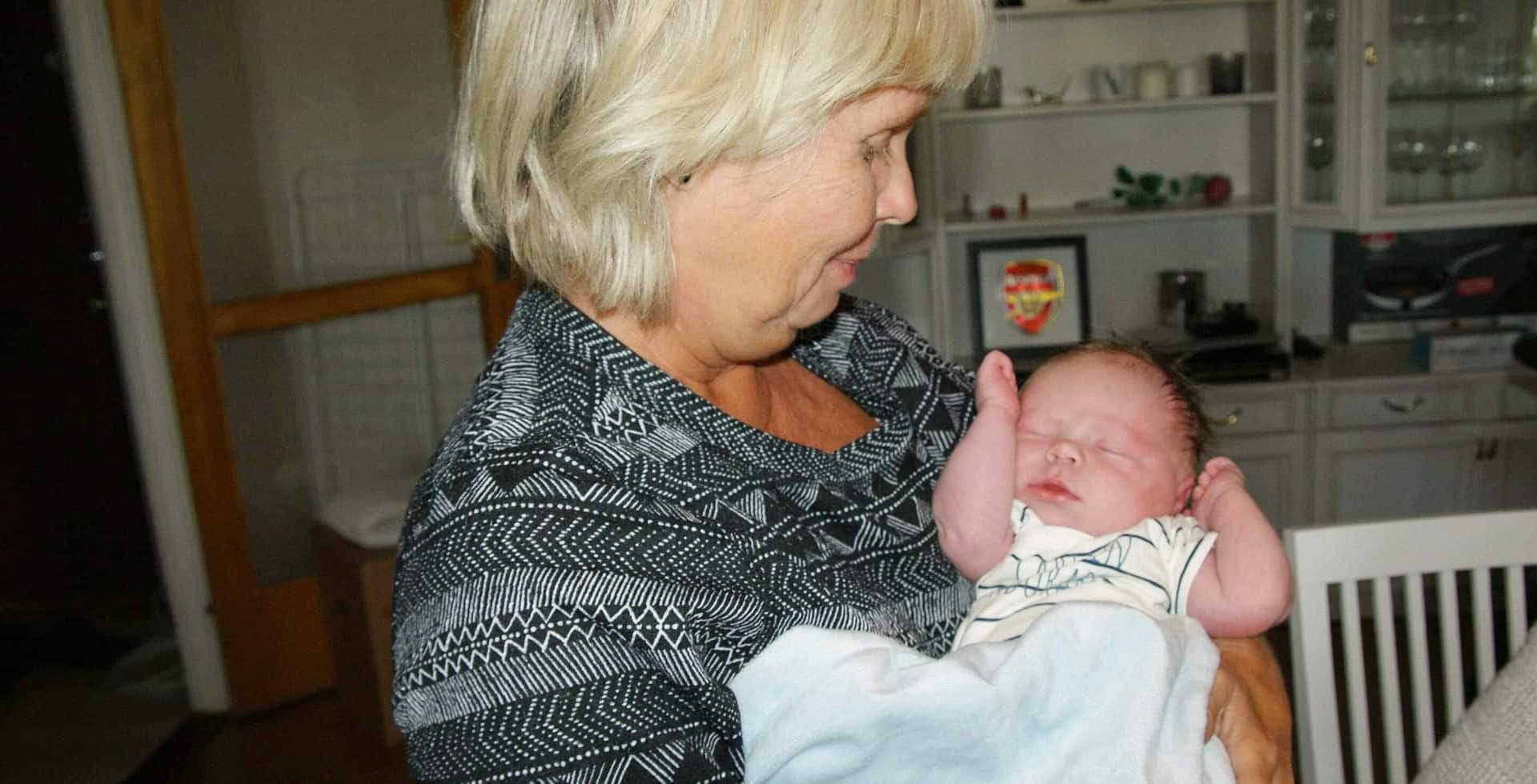Alzheimerdrabbade Ulla står med sitt första barnbarn i famnen.