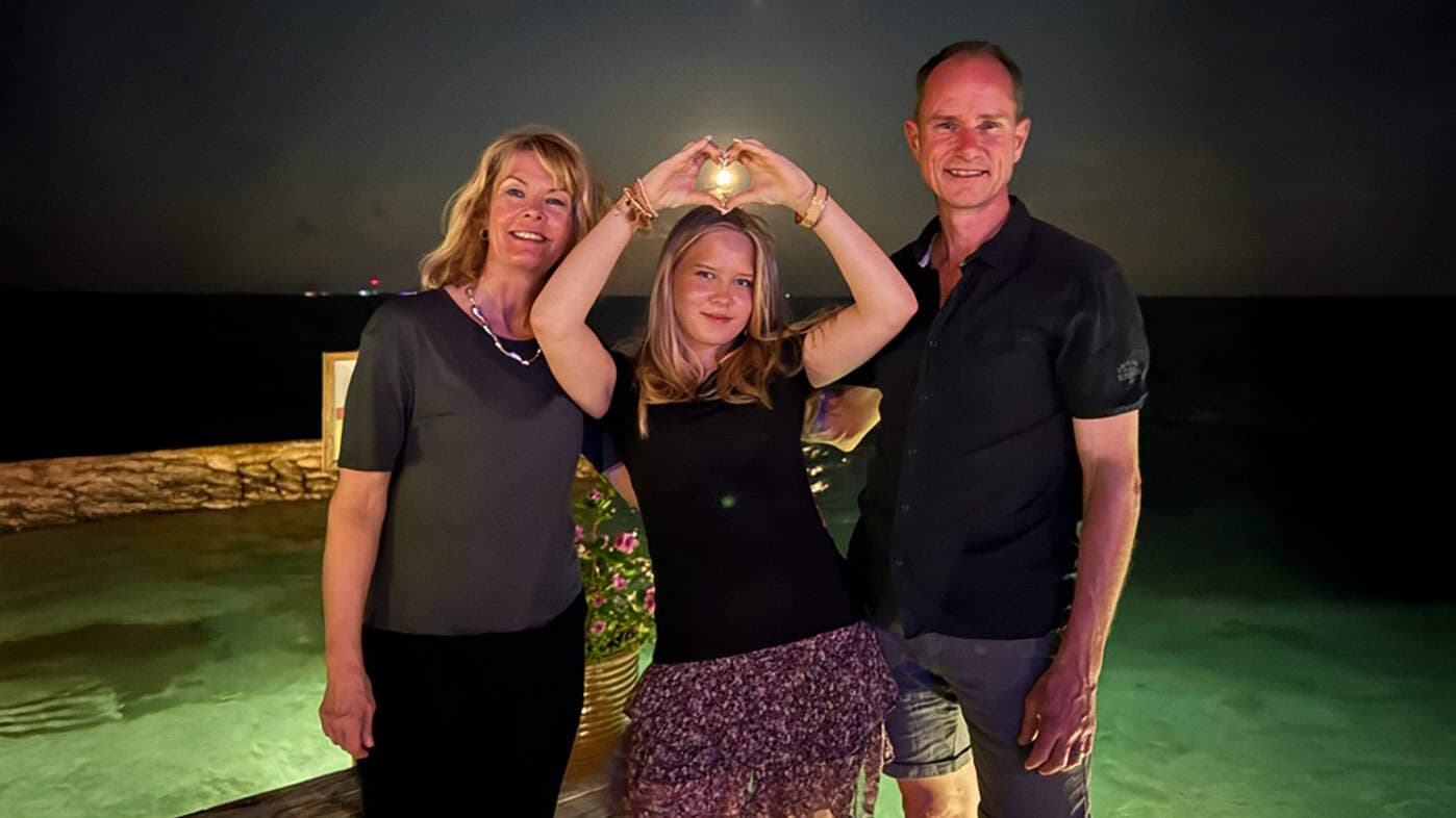 Saga står med sina föräldrar och gör ett hjärta med sina händer.