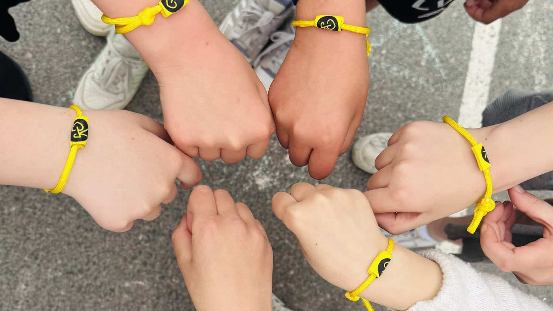 Barn håller in sina händer som bär gula armband med Team Rynkeby logotyp på.