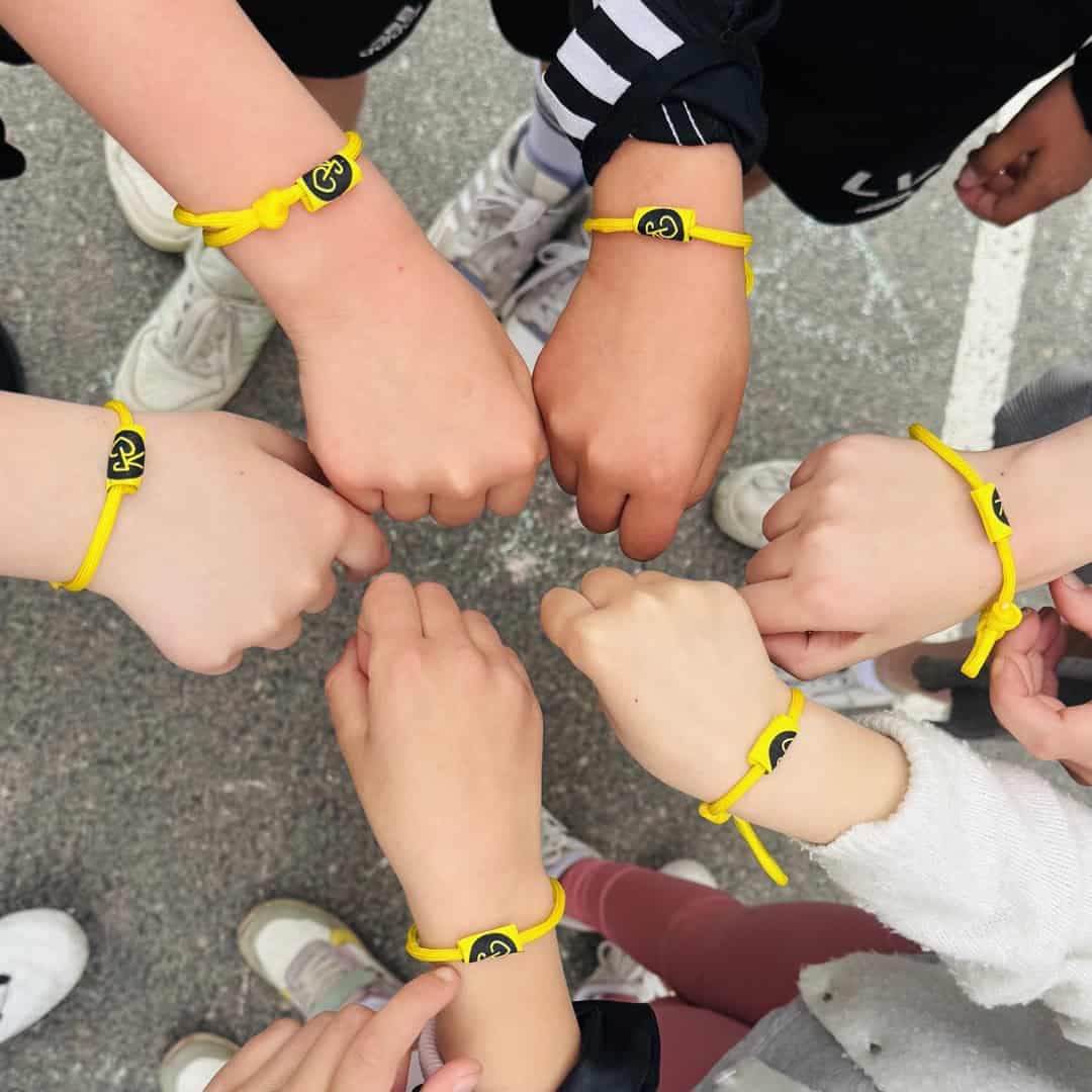 Barn håller in sina händer som bär gula armband med Team Rynkeby logotyp på.