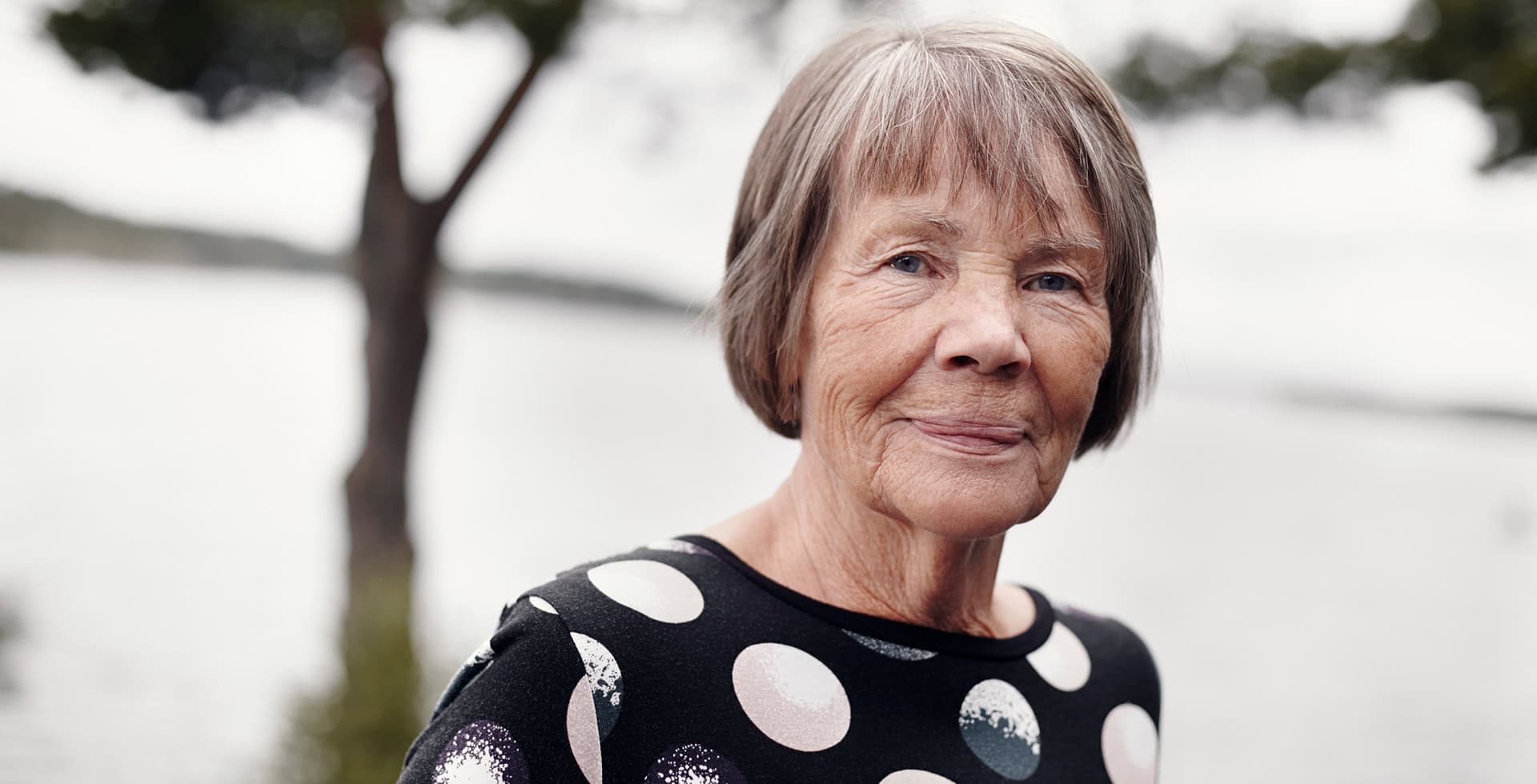 Porträtt av en äldre person som står utomhus vid vatten.