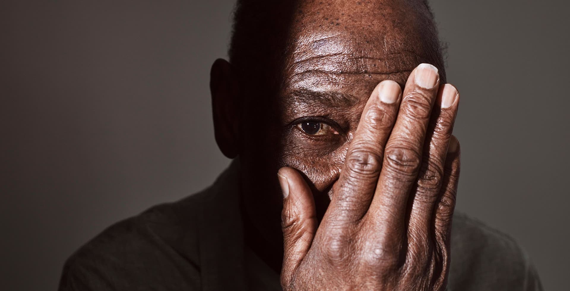 Porträtt av en äldre man som håller handen för ena ögat.